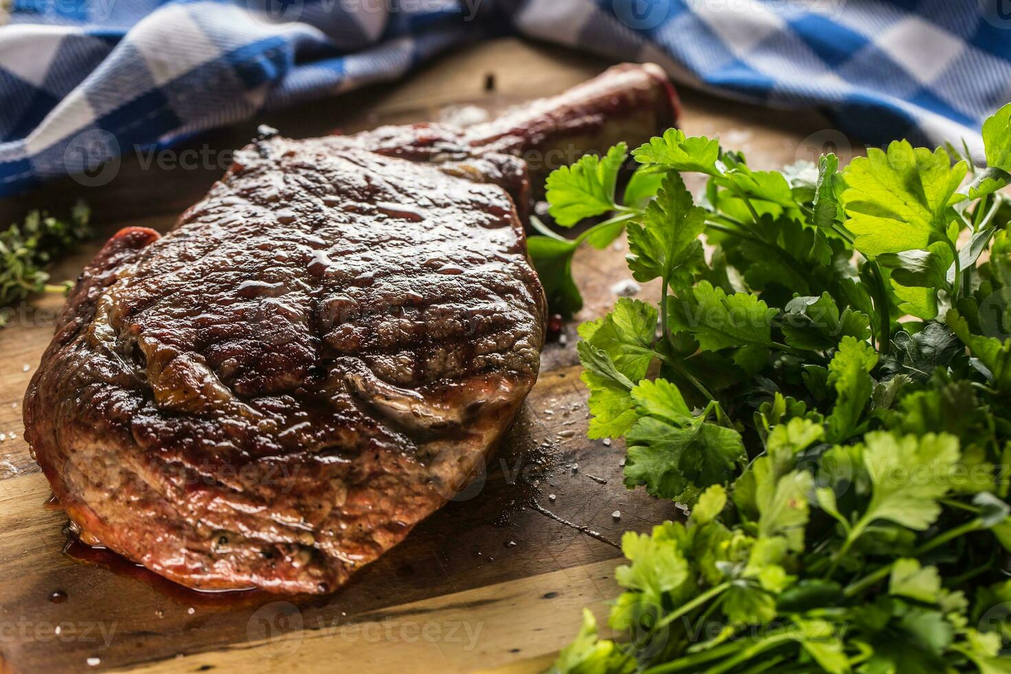 Freshly grilled tomahawk steak on slate plate with salt pepper rosemary and parsley herbs photo