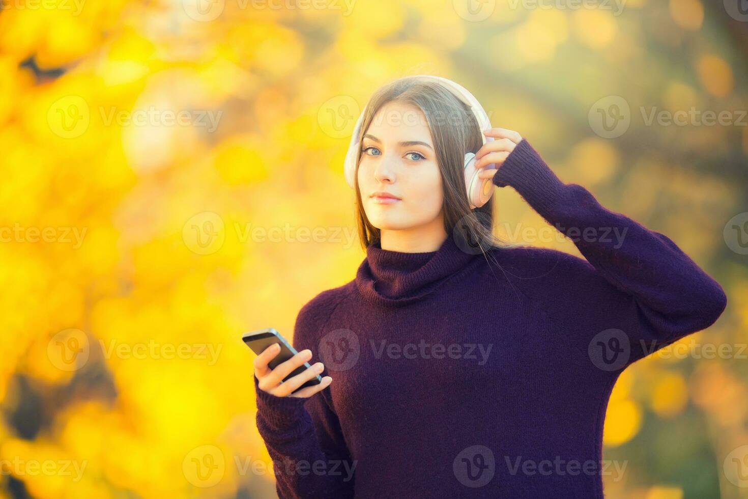 retrato de contento joven niña con auriculares y teléfono inteligente escuchando música en otoño parque foto