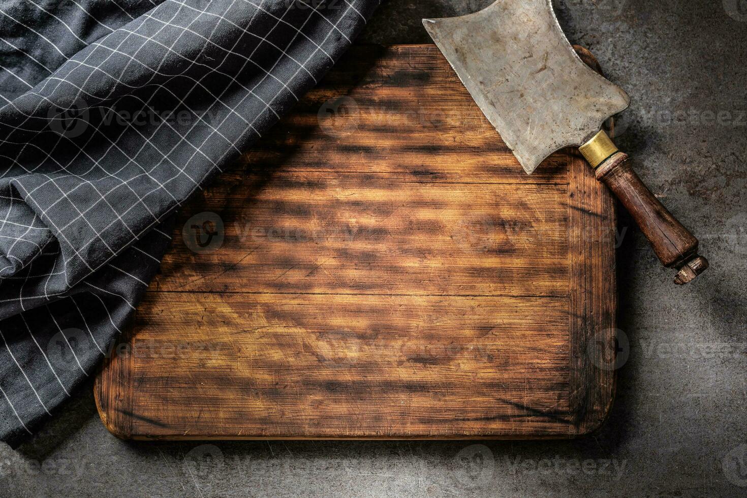 View from above on an empty cutting board, with vintage cleaver and dark checked tea towel on top of it with a dark background photo