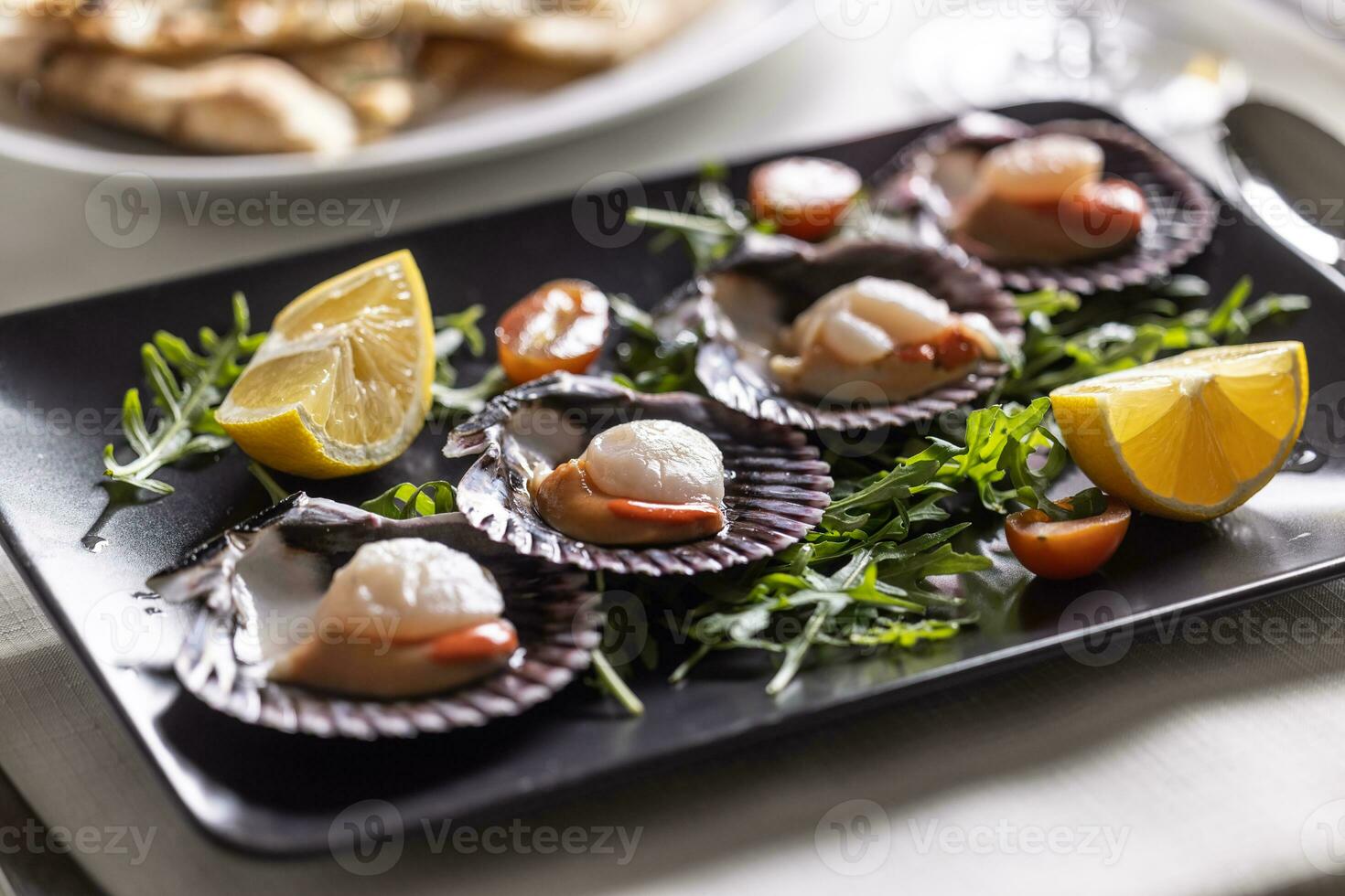 St Jacob scallops served on a dark plate with wedges of lemon and rocket salad photo