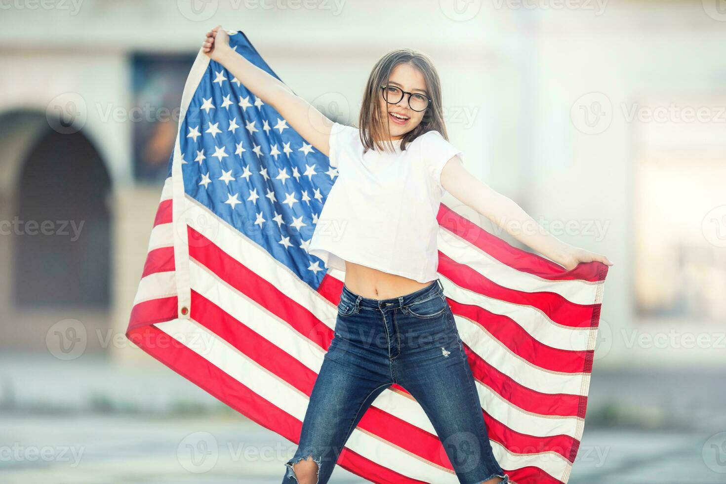 Happy young american school girl holding and waving in the city with USA flag photo