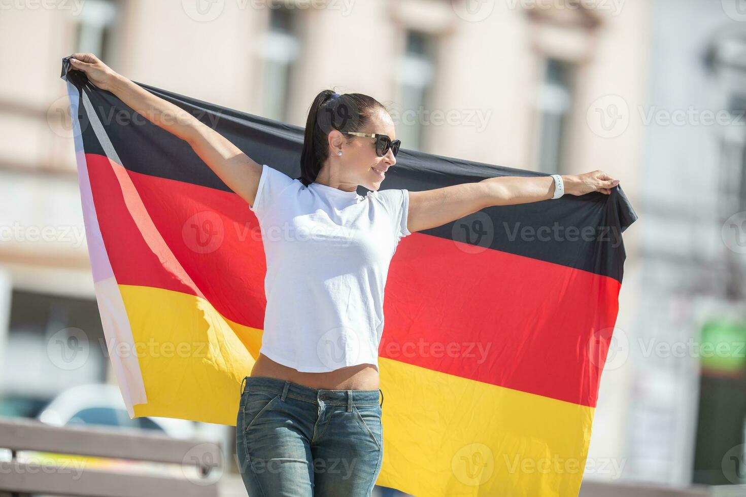 hermosa sonriente niña en Gafas de sol sostiene un alemán bandera detrás su al aire libre foto