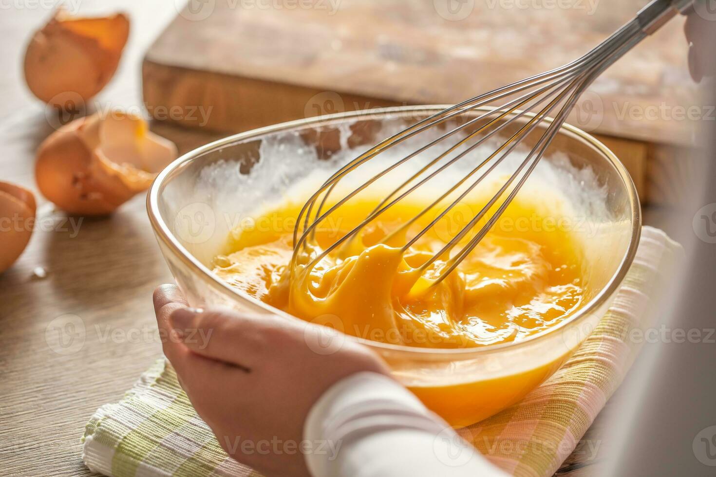 Detail of eggs being whisked in a bowl placed on a towel and wooden table photo