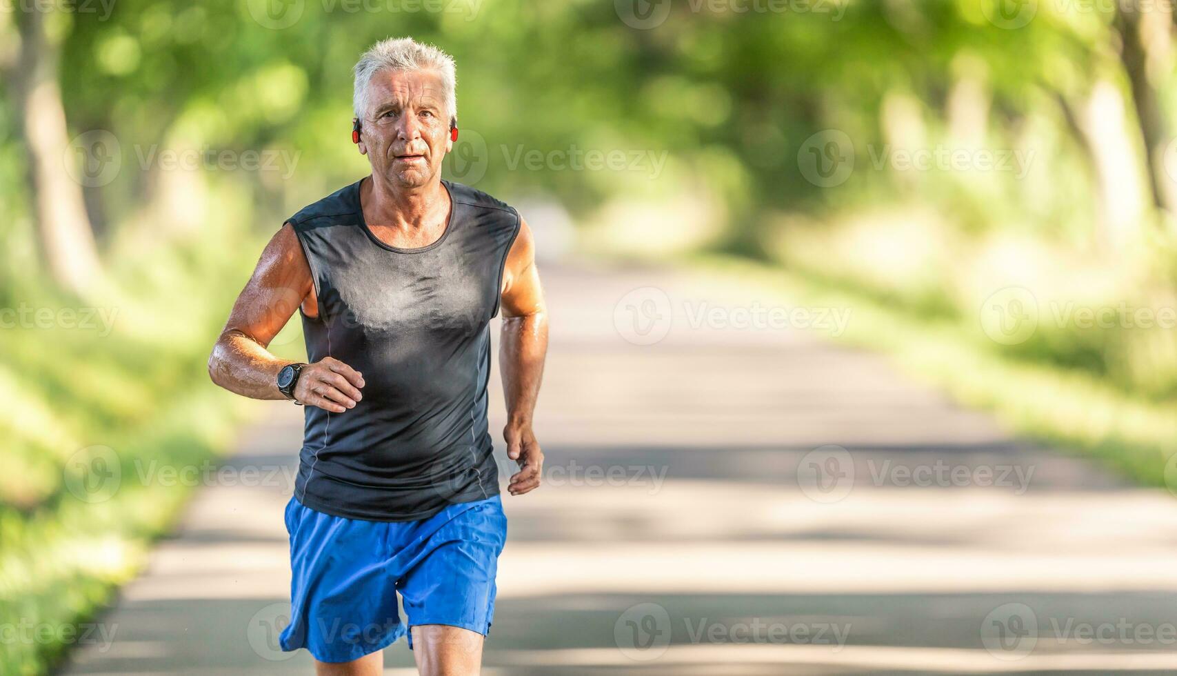 Fit old man in shorts and shirt without sleeves runs outdoors in the nature photo