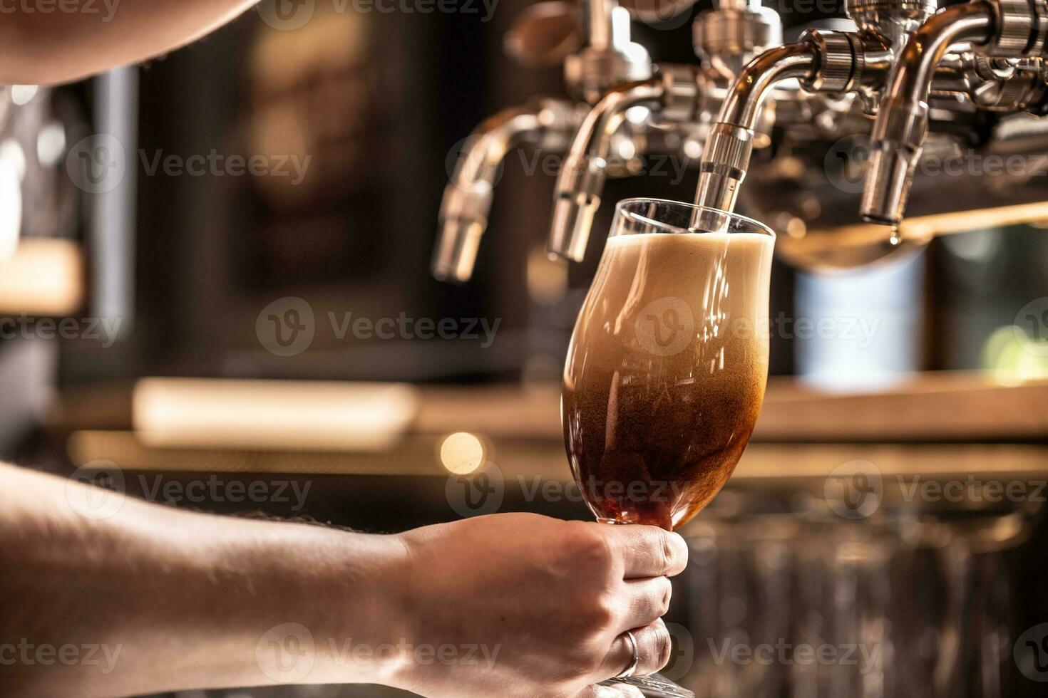 Dark beer being tapped into  a glass with rich foam formation on top photo