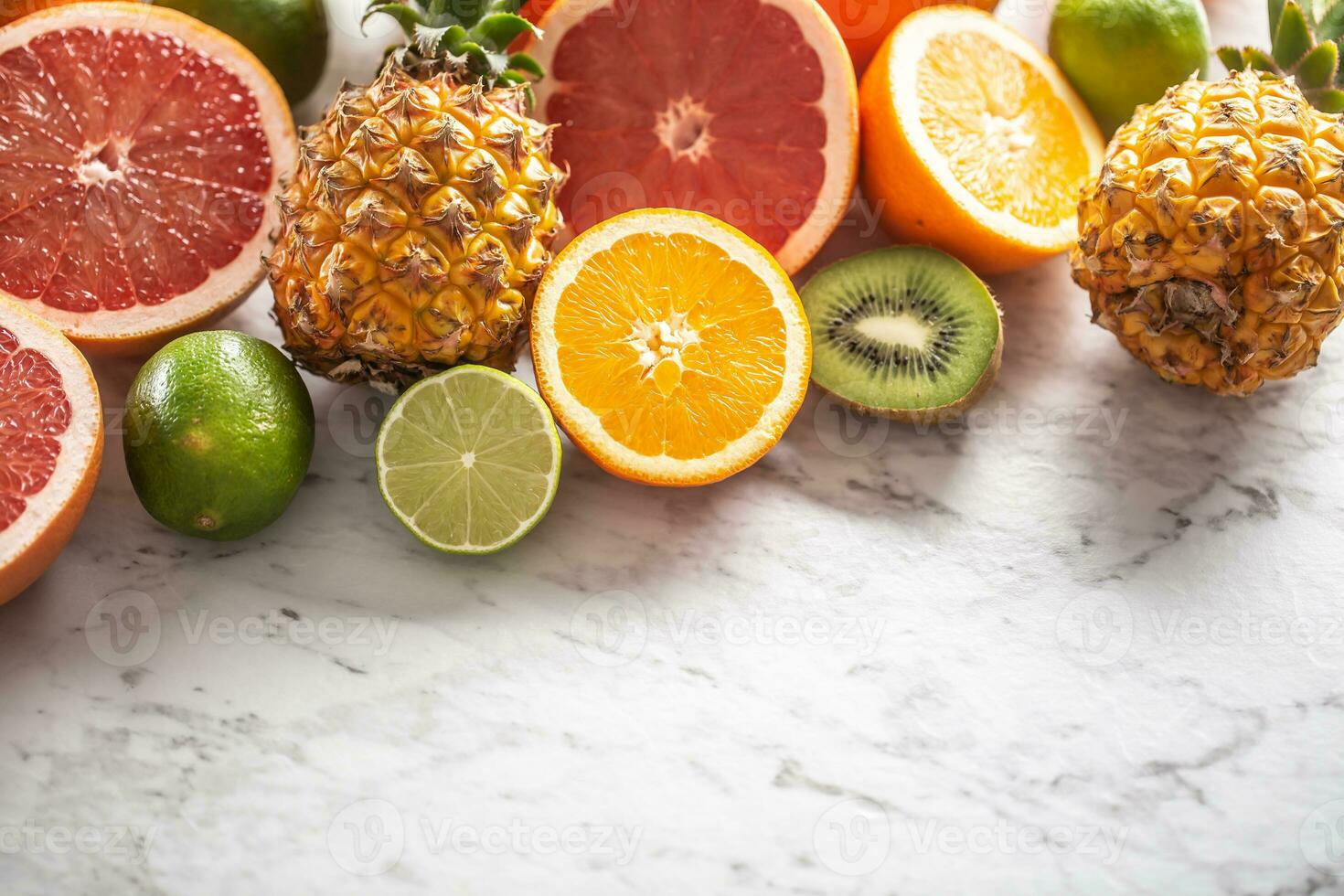 Various citruses such as oranges, limes, grapefruits, as well as pineapples on a marble surface photo