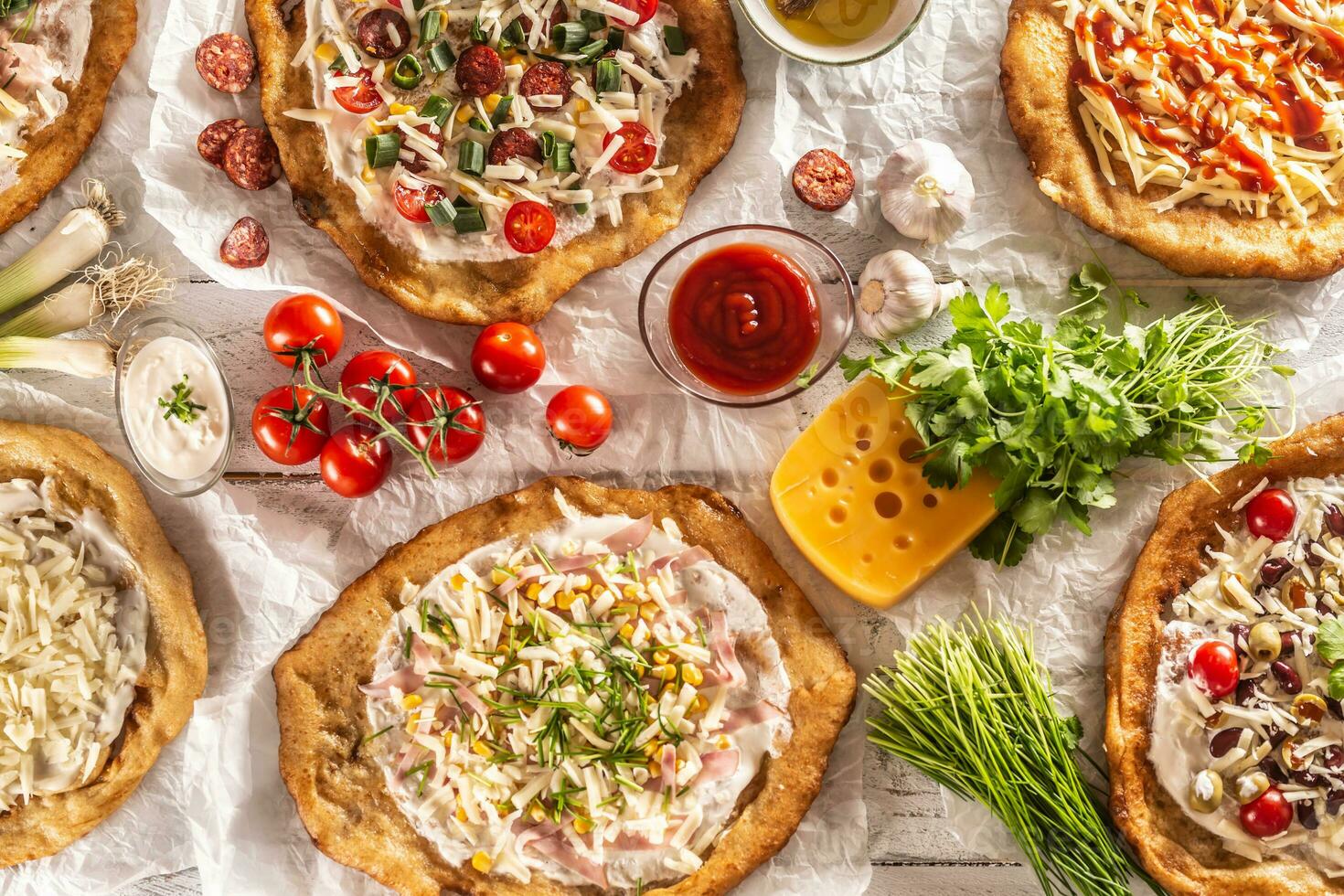 A close up a set of hungarian traditional langos with crusty garlic edges served with vegetables, cream sausages, herbs, grated, cheese, ketchup and dips photo
