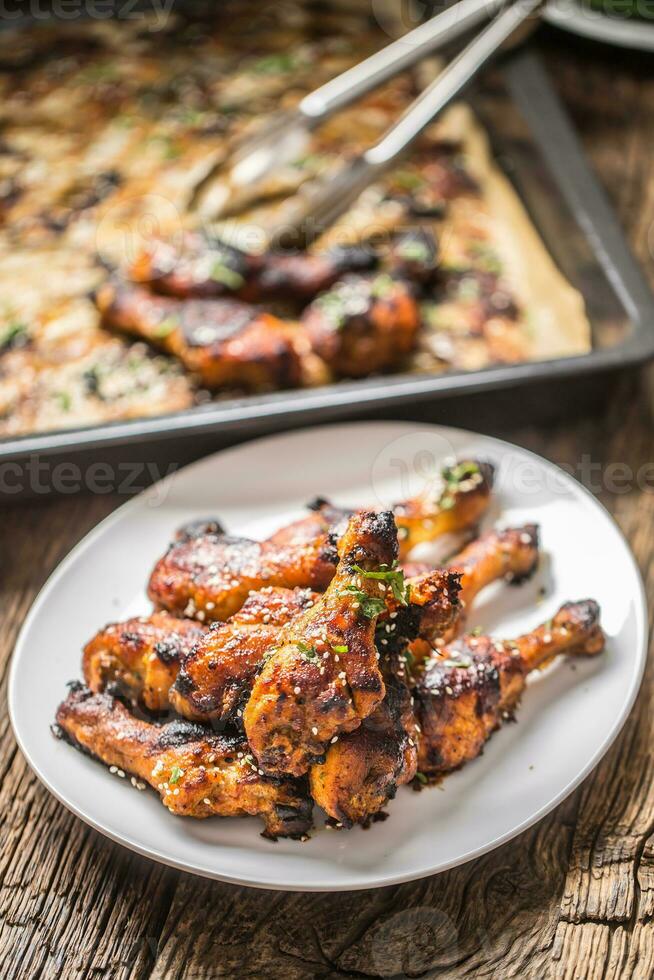 Grilled hicken legs BBQ with spices herbs and sesame on baked paper. Roasted poultry meal on white plate photo