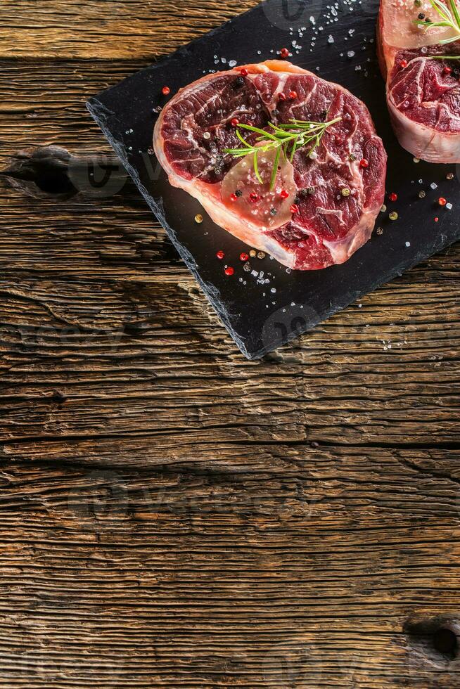 Two pieces raw beef shank on slate board and wooden table. photo