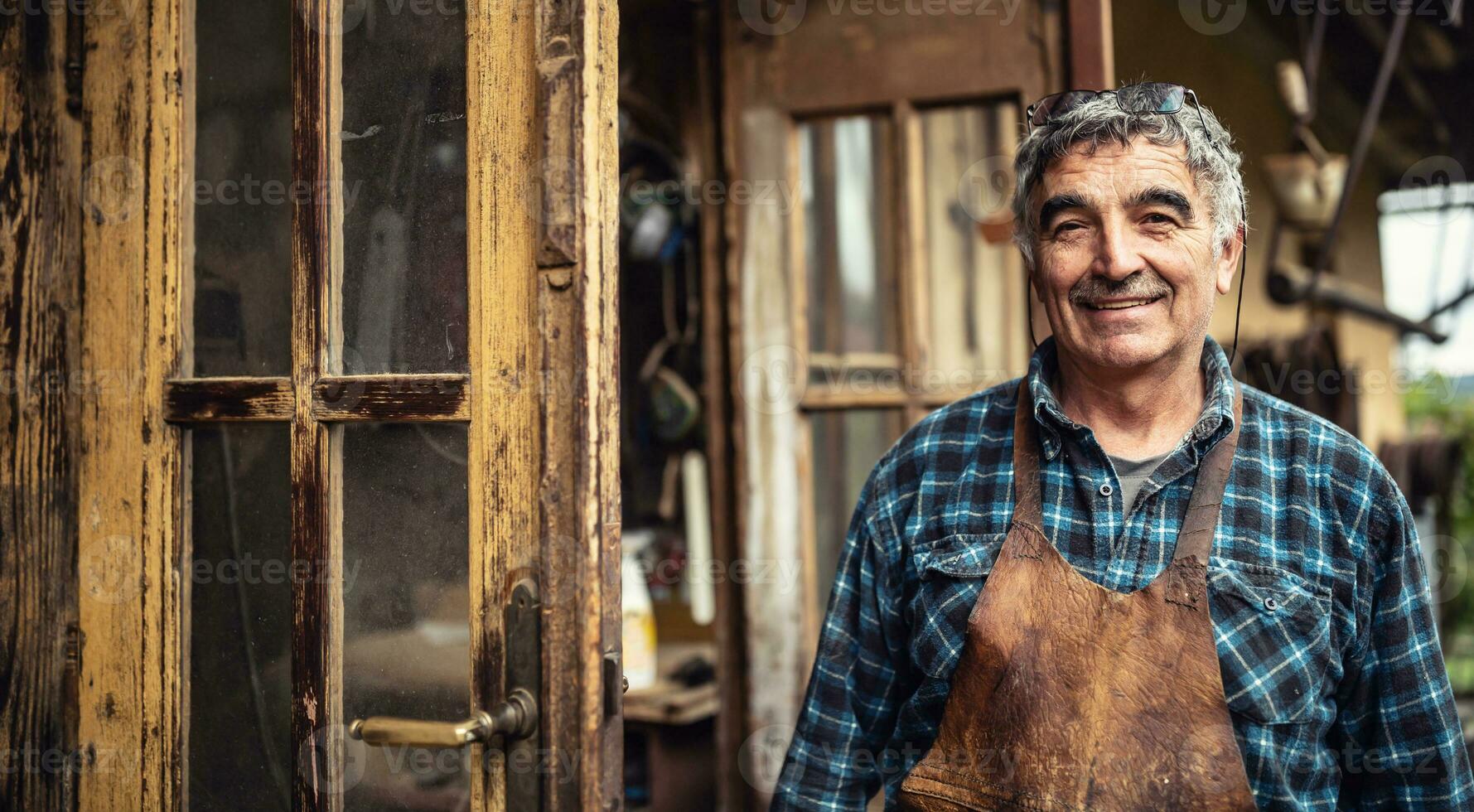 Aged craftsman standing and smiling in front of his rustic workshop photo