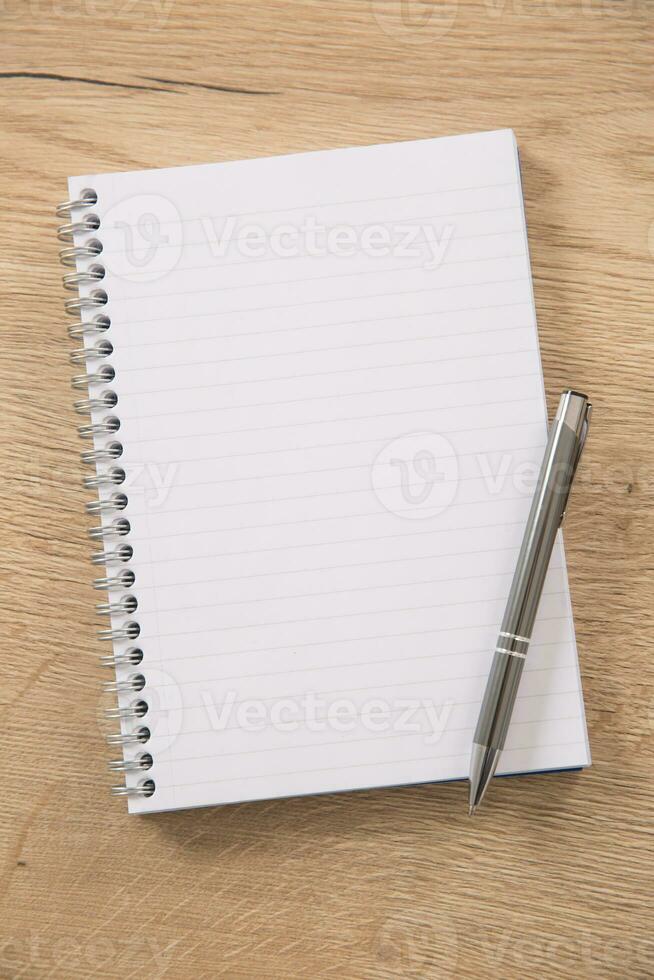 White lined notepad with a metal ring wire binding and a silver pen opened on a wooden surface photo