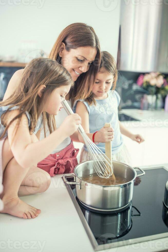 mamá con dos joven Gemelos hijas en el cocina Cocinando espaguetis foto