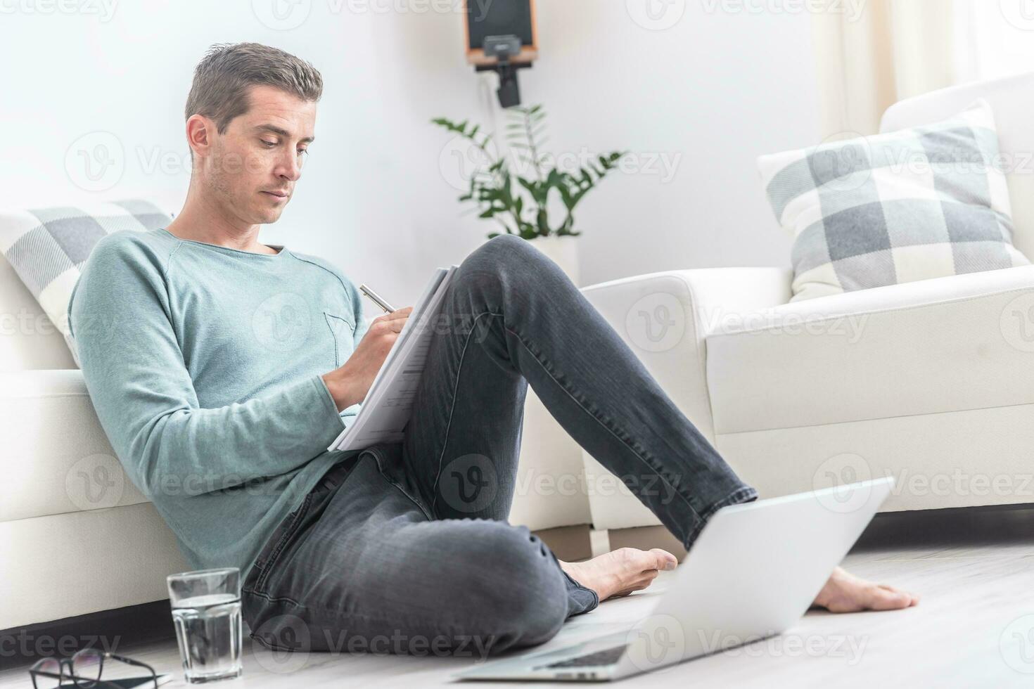 Man working from home writes down on paper while sitting on the floor photo