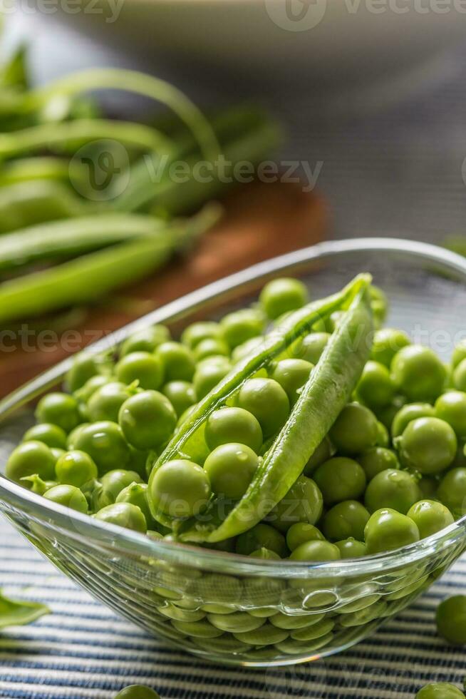 Fresh green pea seeds in bowl on kitchen table photo