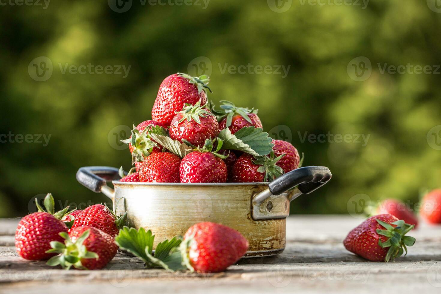 Fresh ripe strawberries in vintage kitchen pot on old garden table photo