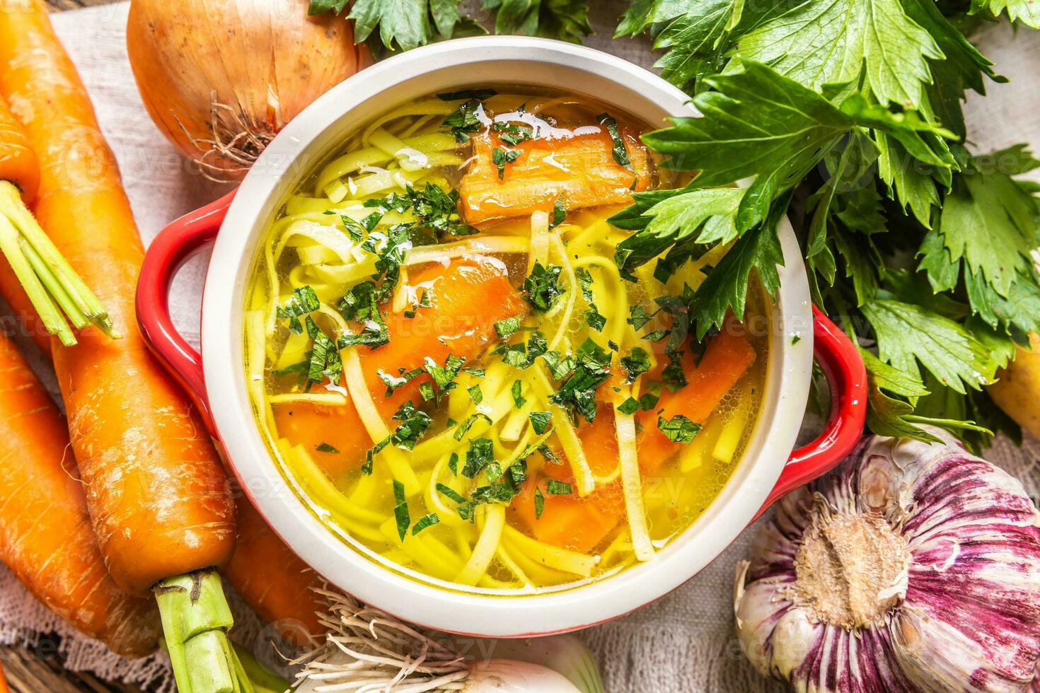 Chicken soup broth in a vintage bowl with homemade noodles carrot onion celery herbs garlic and fresh vegetables. photo