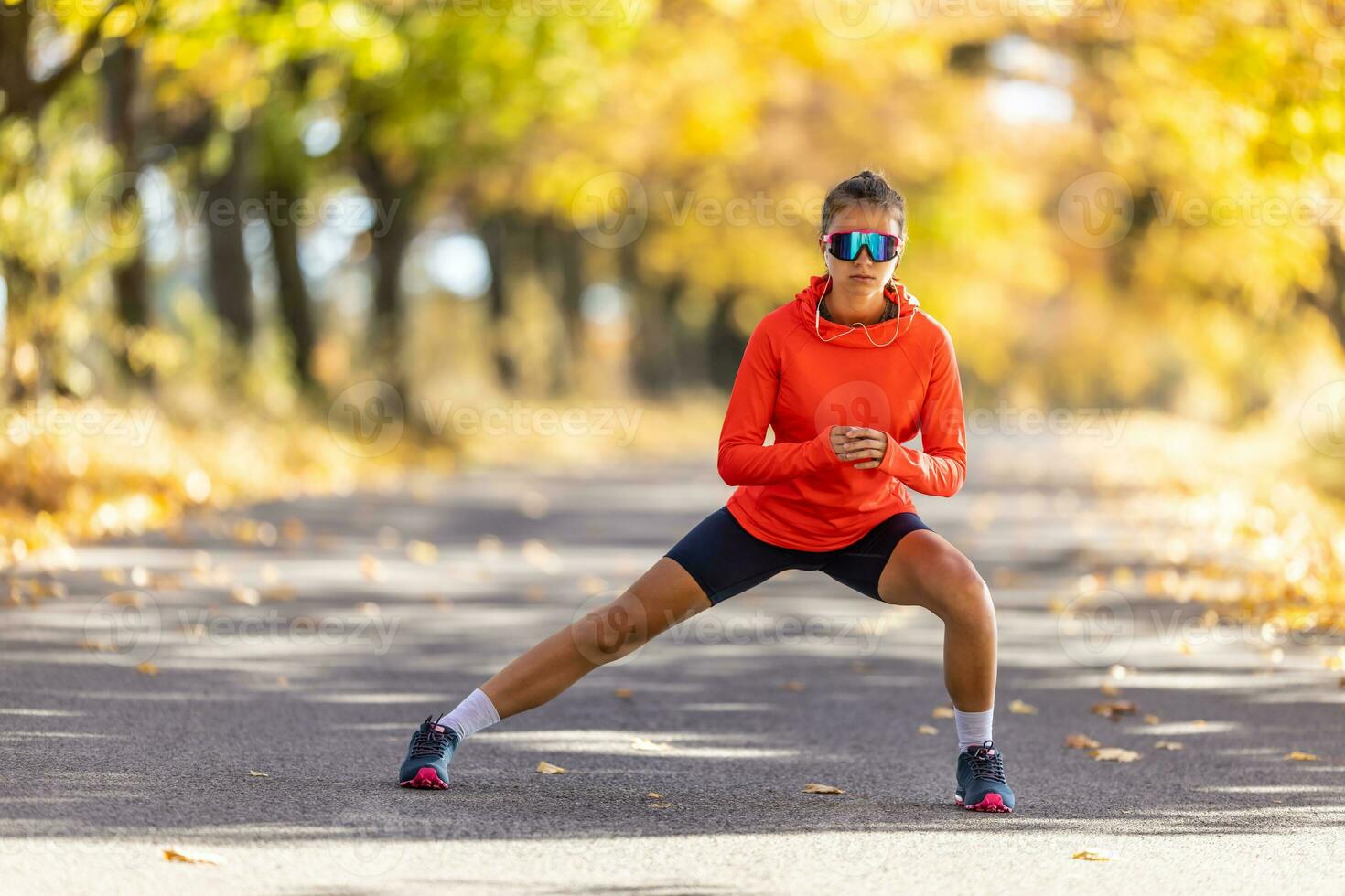 Young female athlete in sportswear is warming up before running in the autumn park photo