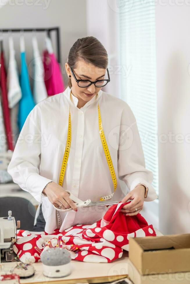 Female tailor wearing glasses cuts polkadot fabric in the workshop with scissors photo
