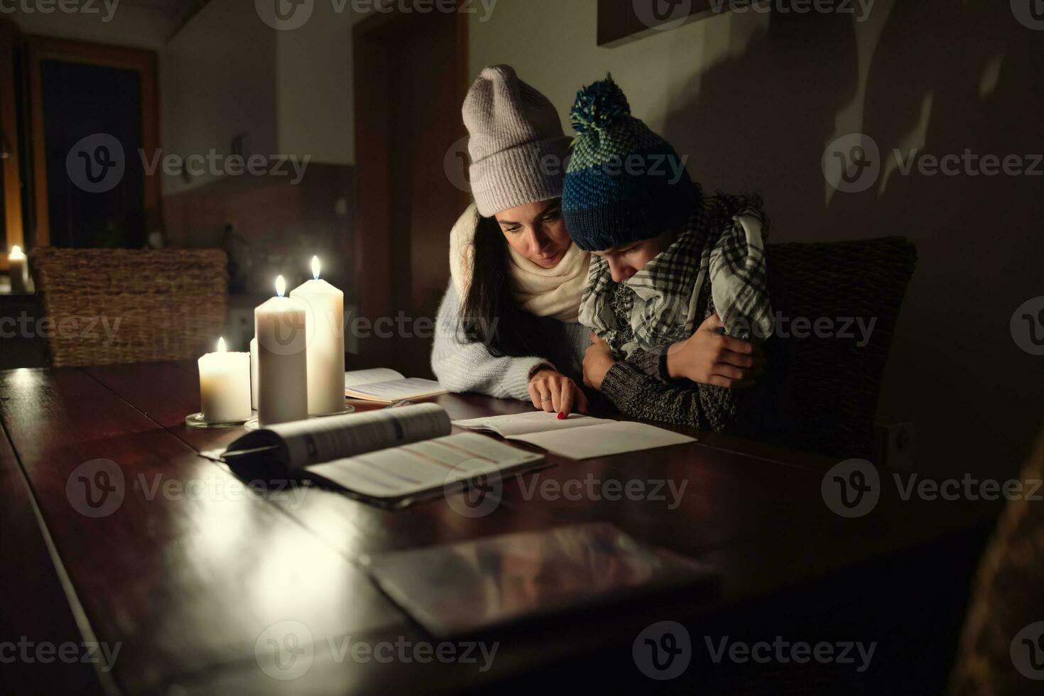 Woman and her son sit at the tabel at home dressed in winter caps and shawls shivering from cold due to European energy crisis in winter photo