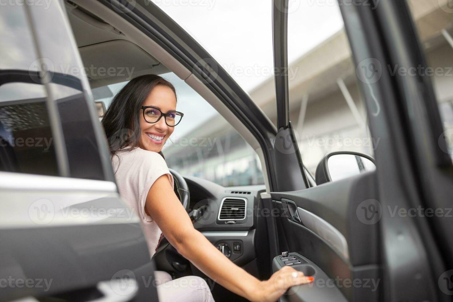 Smiling female driver opens the door on a righ-hand driven car in front of a shopping centre photo