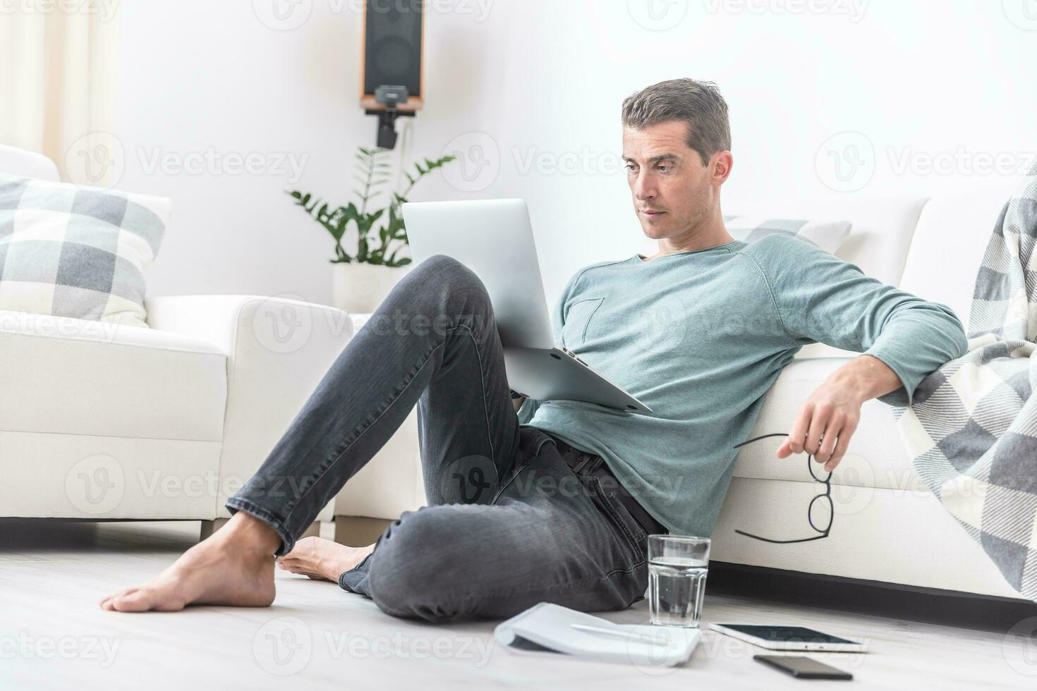 masculino persona de libre dedicación se sienta descalzo en el vivo habitación piso trabajando en un ordenador portátil foto