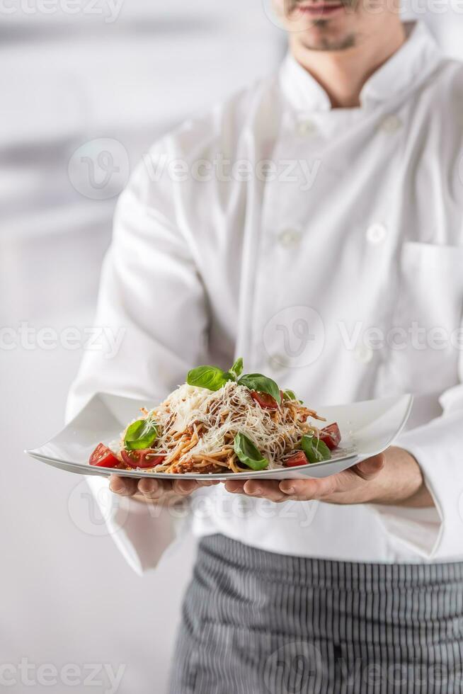 Chef in restaurant kitchen holding plate with italian meal spaghetti bolognese photo