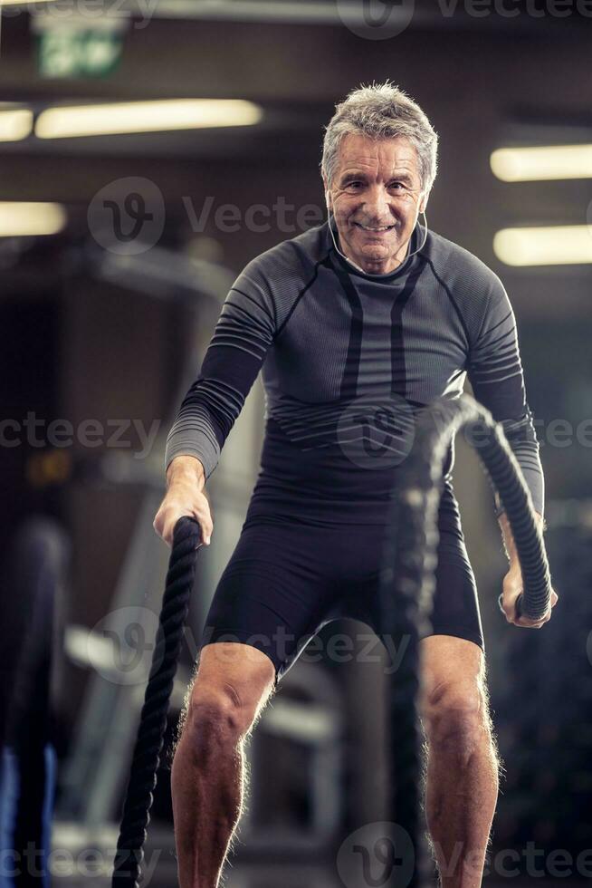 más viejo hombre con auriculares ejercicios con cuerdas en un aptitud formación centrar foto