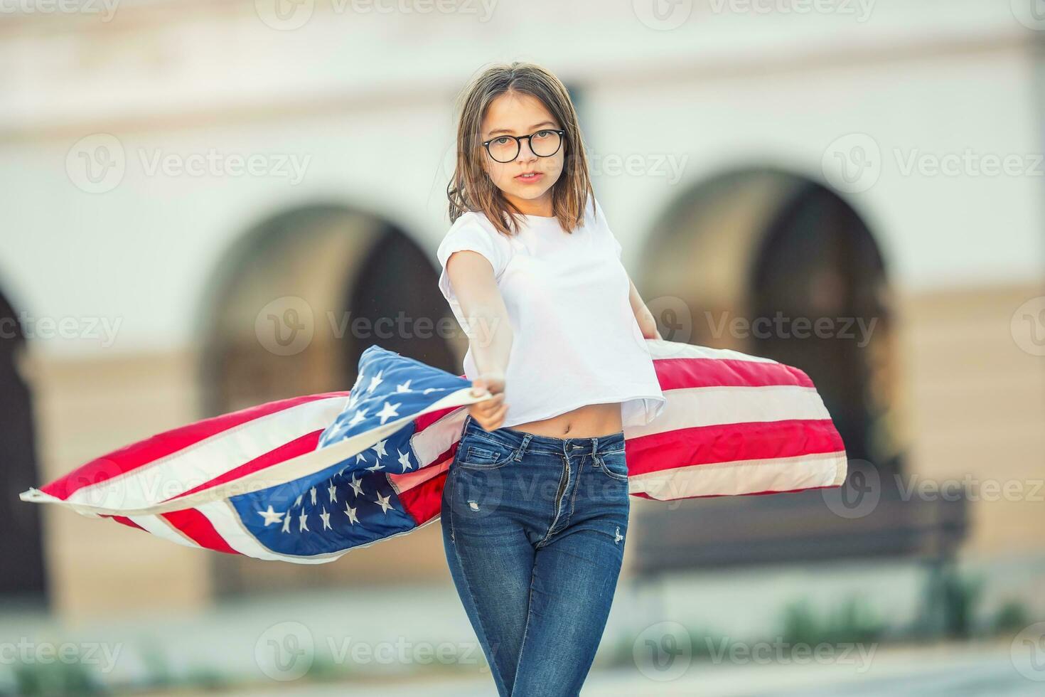 Happy young american school girl holding and waving in the city with USA flag photo