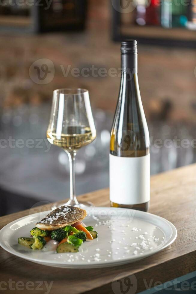 sano pescado cocido con al vapor vegetales servido en un plato siguiente a un botella de blanco vino foto