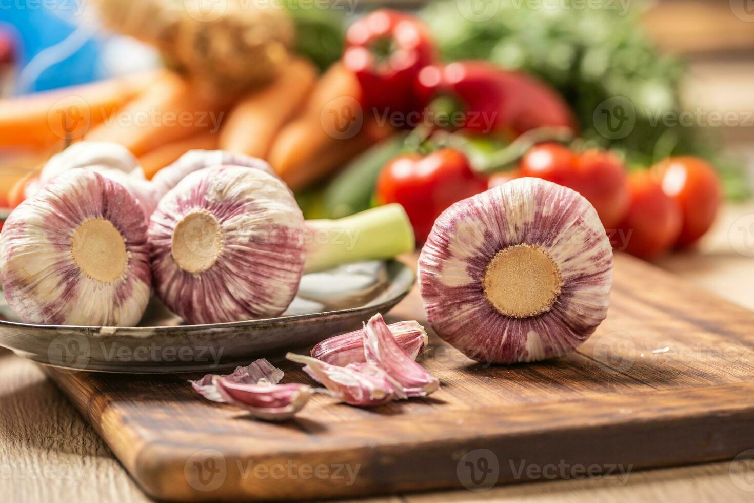 Five heads of garlic on a cutting board with various vegetables in the background photo