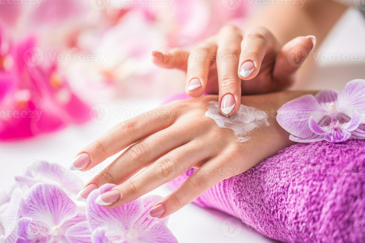 hermosa hembra manos aplicando mano crema. púrpura toalla y orquídea decoración. sano concepto - uñas spa piel cuidado y bienestar foto
