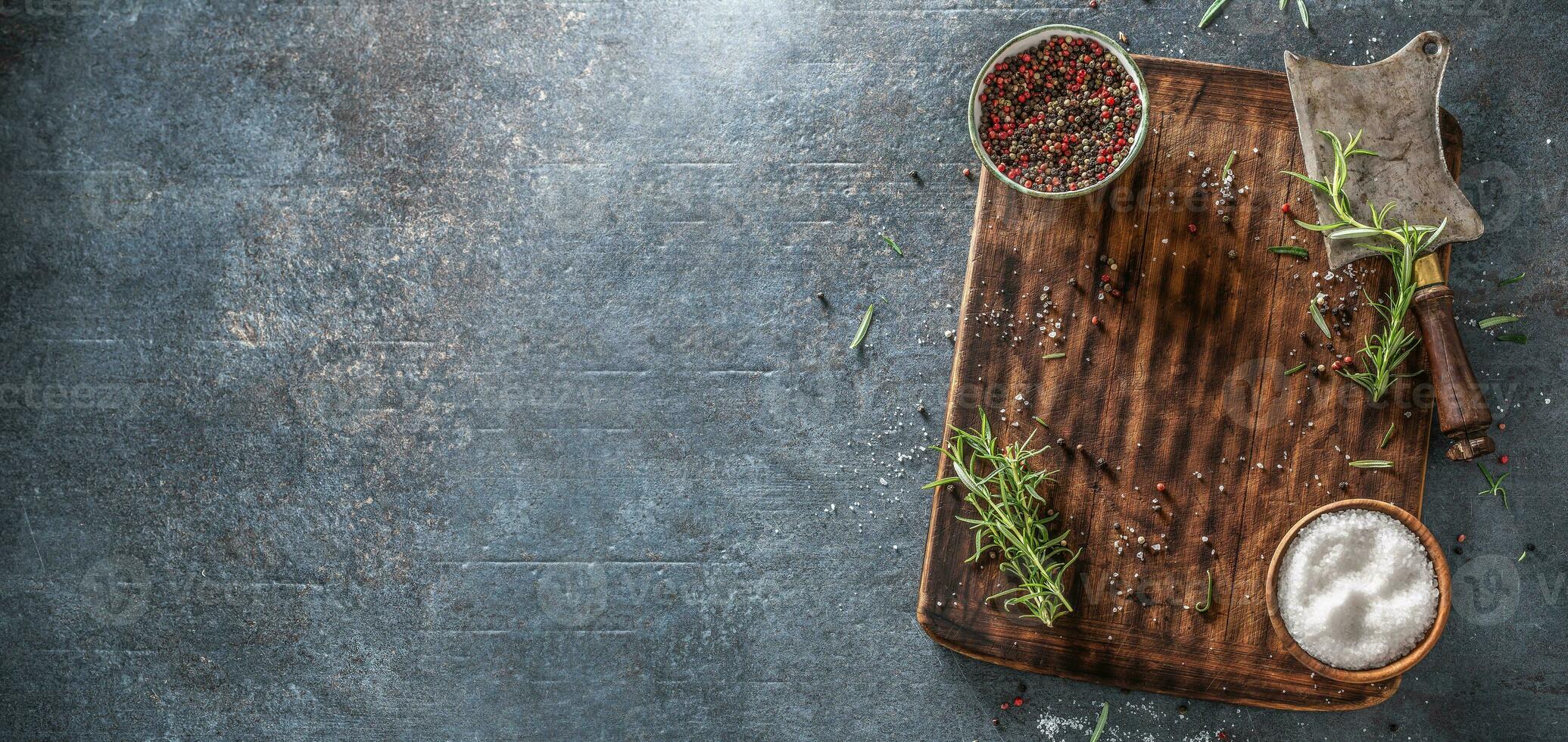 Top view of rectangular chopping board with preps and seasonings covering the right third of a dark blue metalic background photo