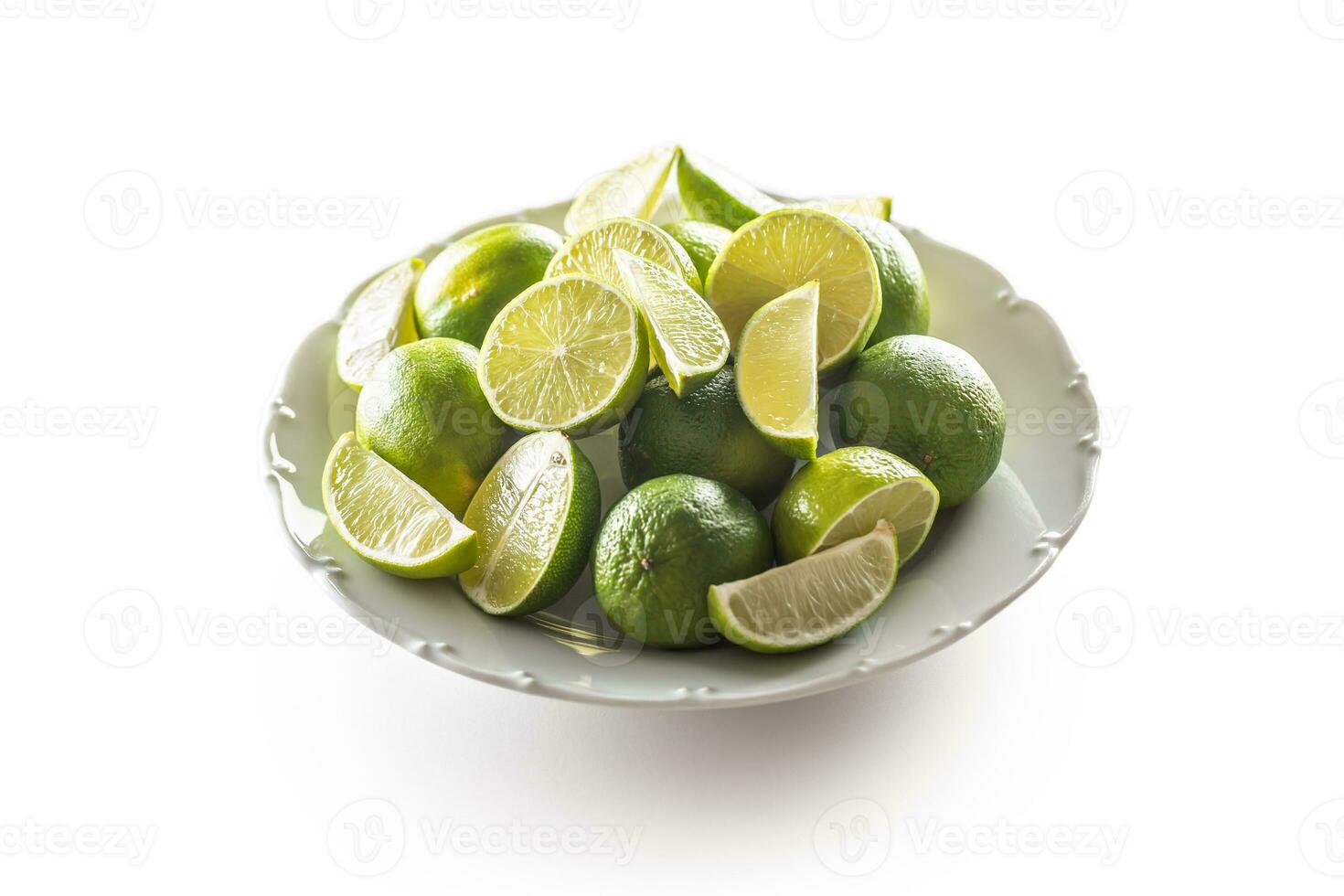 Plate full of fresh whole and wedged limes on a white background photo