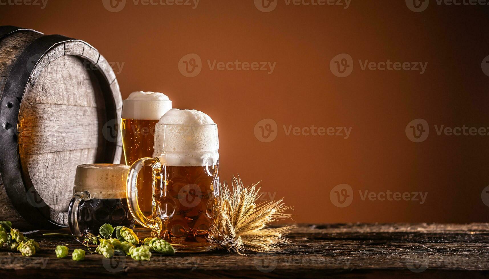 Three glasses with draft beer in front of a wooden barrel. Decoration of barley ears and fresh hops photo