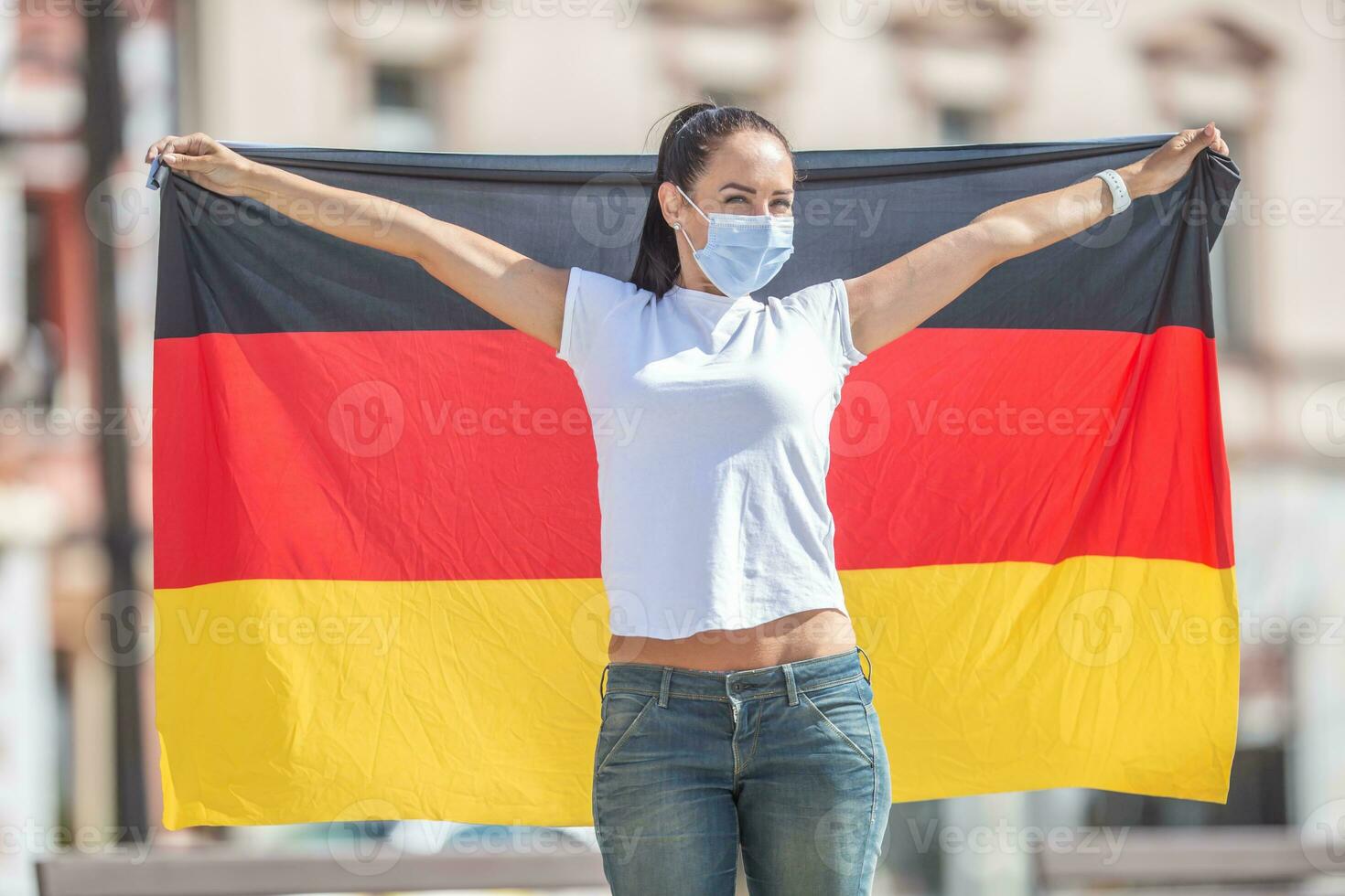 Woman wearing a face mask holds a flag of Germany behind her photo