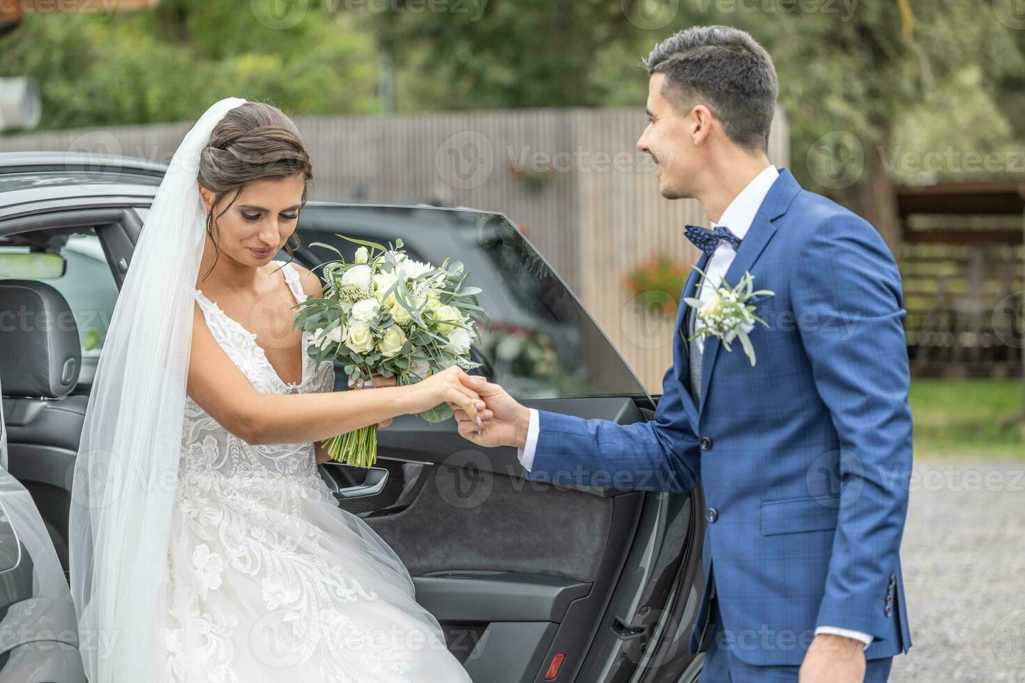 Husband from a just married couple gives a heloing hand to his wife getting out of the car. photo