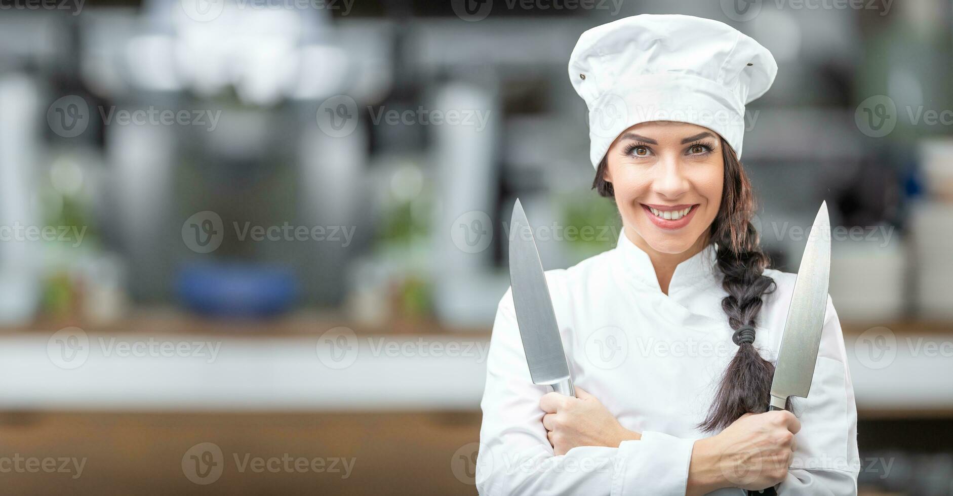 guapo hembra cocinero soportes en el cocina participación dos cuchillos sonriente a el cámara foto