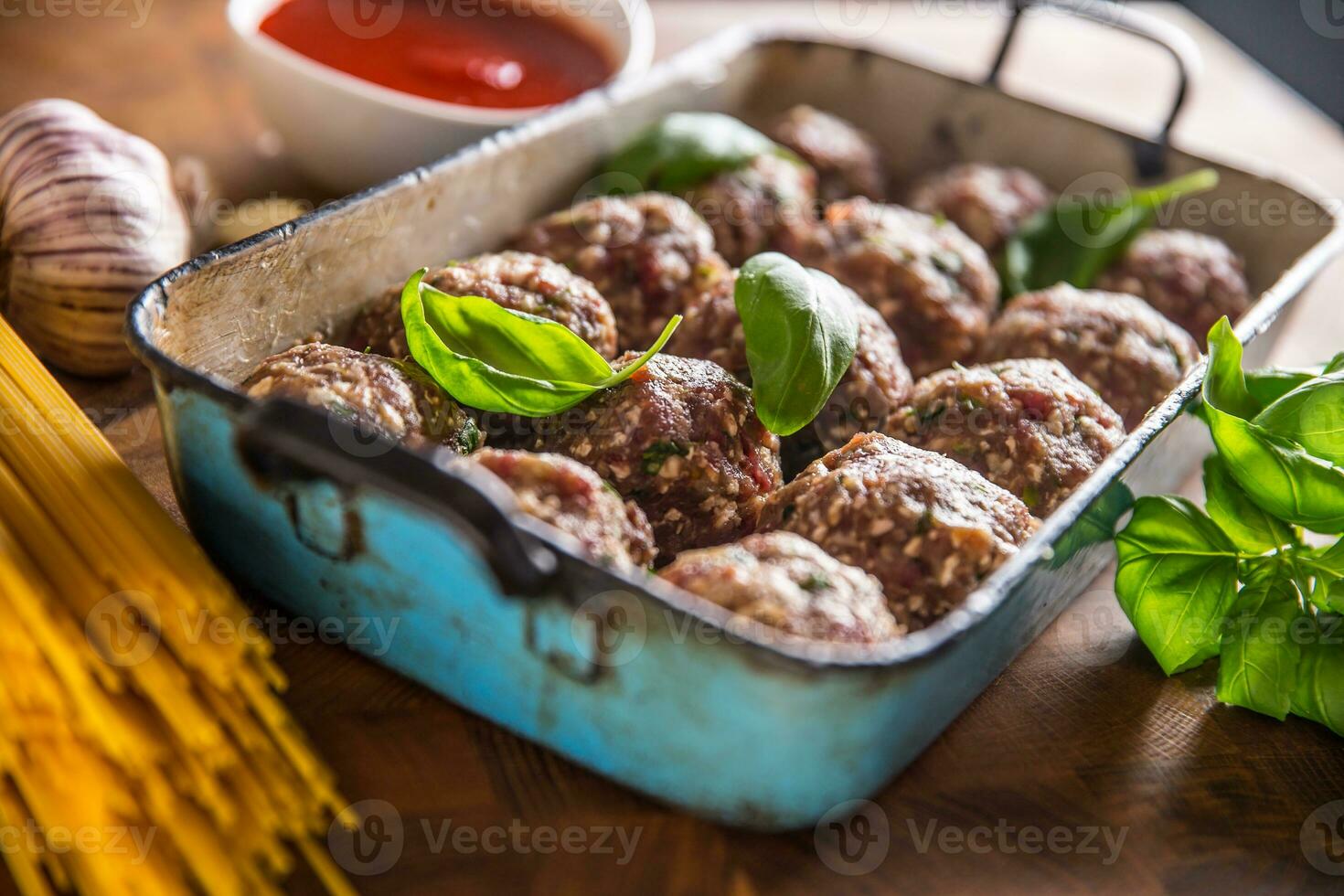 Raw feef meat balls basil tomato sauce garlic and spaghetti on butcher board photo