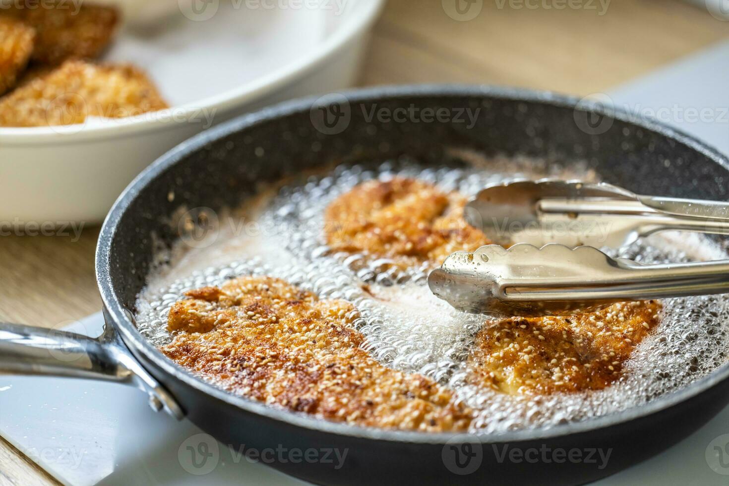 Detail of pan with schnitzels bubbling in hot oil and pliers taking them out photo