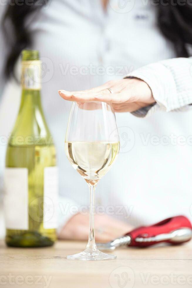Female holding a hand above the glass of white wine with bottle and wine opener next to it photo