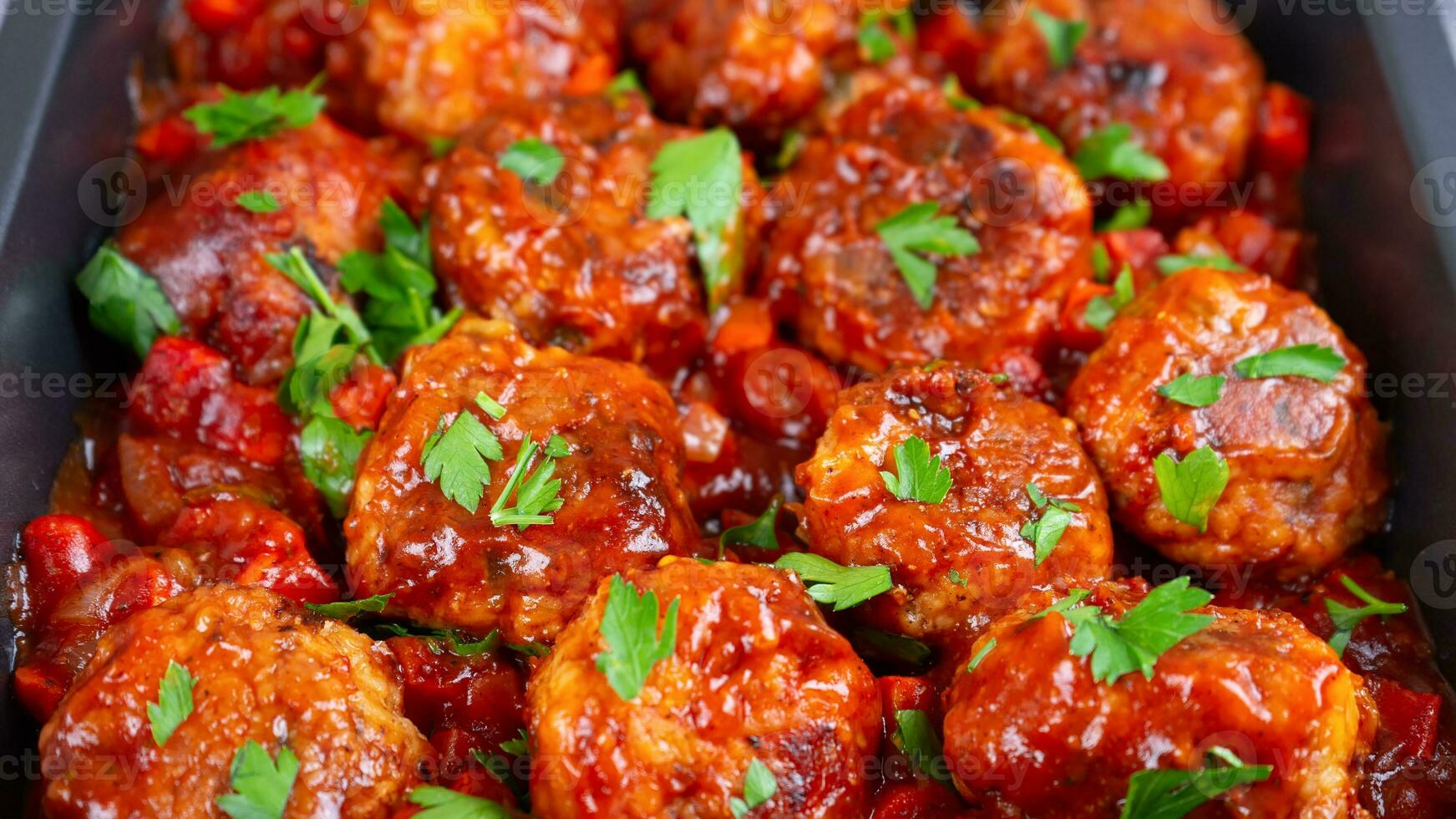 Homemade meatballs with tomato sauce and fresh parsley in black pan close up photo