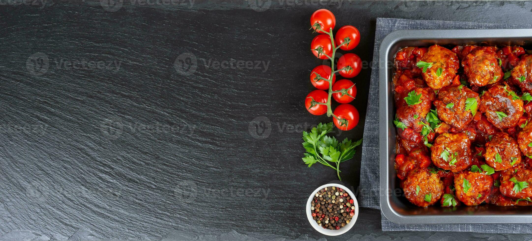 Homemade meatballs with tomato sauce and spices served in black pan on black slate background photo