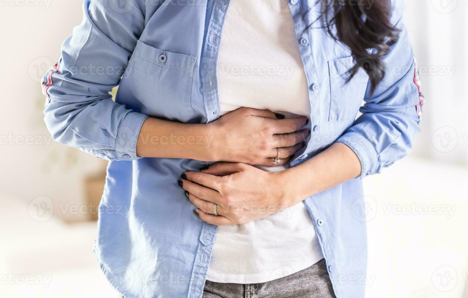 Detail of woman holding stomach by both hands in pain of abdominals photo