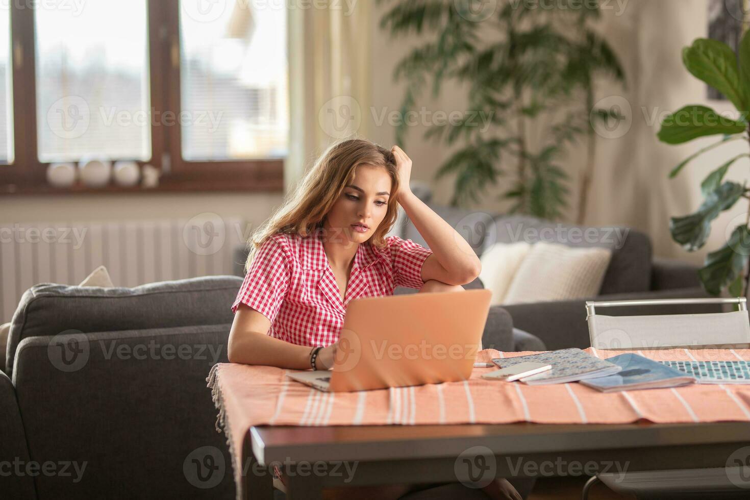 Exhausted blonde student having an online class at home while dreaming about sleeping on the sofa behing her. photo