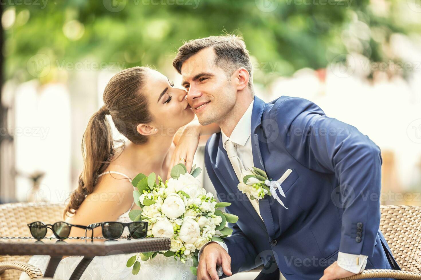 Loving bride kissing her charming huband. They wear wedding robes and hold beautiful bouquet photo