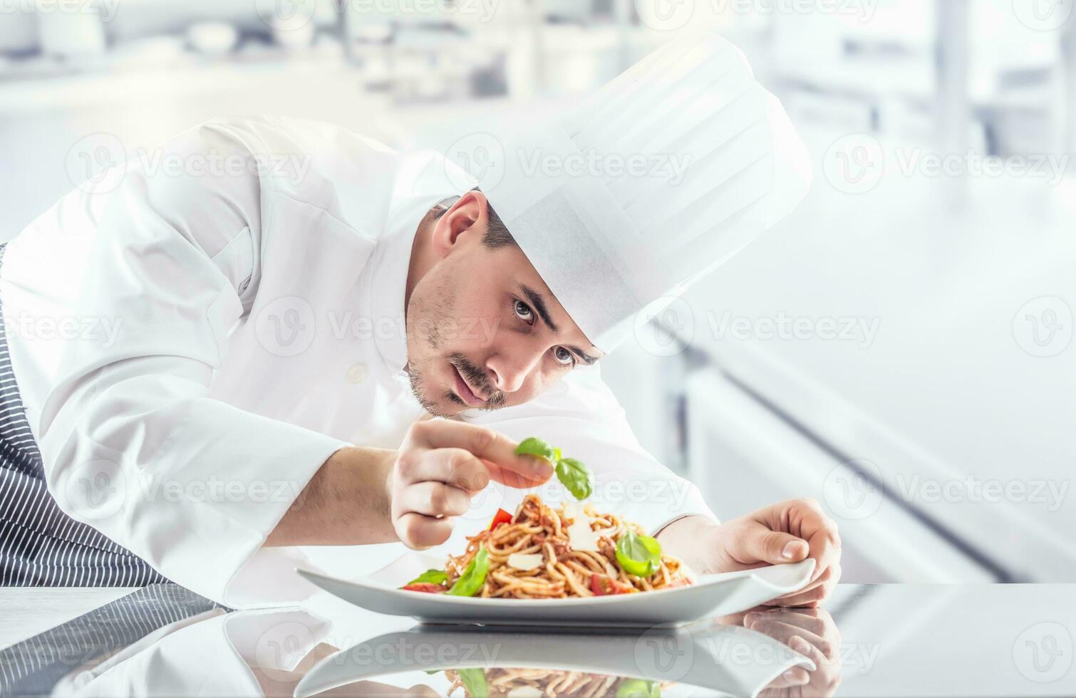 Chef in restaurant kitchen prepares and decorates meal with hands.Cook preparing spaghetti bolognese photo