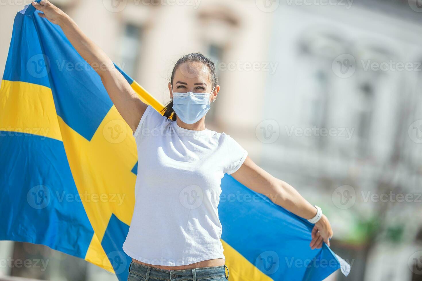 Swedish female fan in a facemask holds a flag behind her back photo