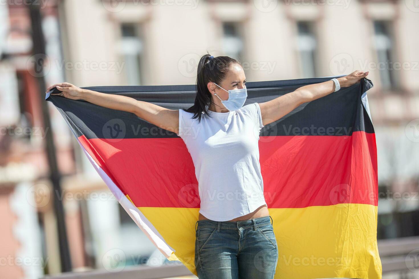Woman wearing a face mask holds a flag of Germany behind her photo