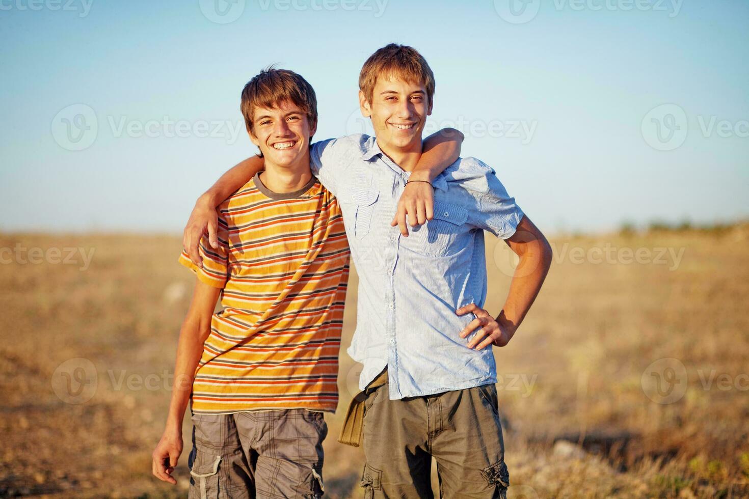 two boys standing in a field with their arms around each other photo