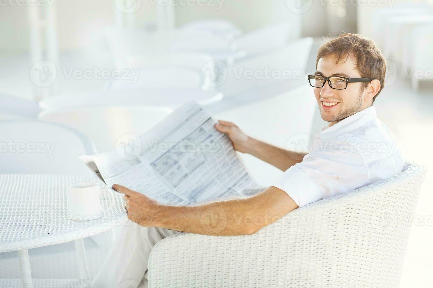 a man in glasses reading a newspaper while sitting at a table photo